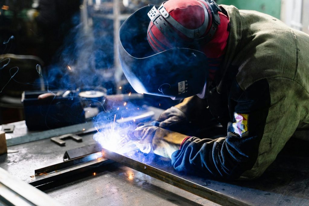 Photo by Pavel Chernonogov A welder works on metal fabrication indoors, creating bright sparks and smoke.